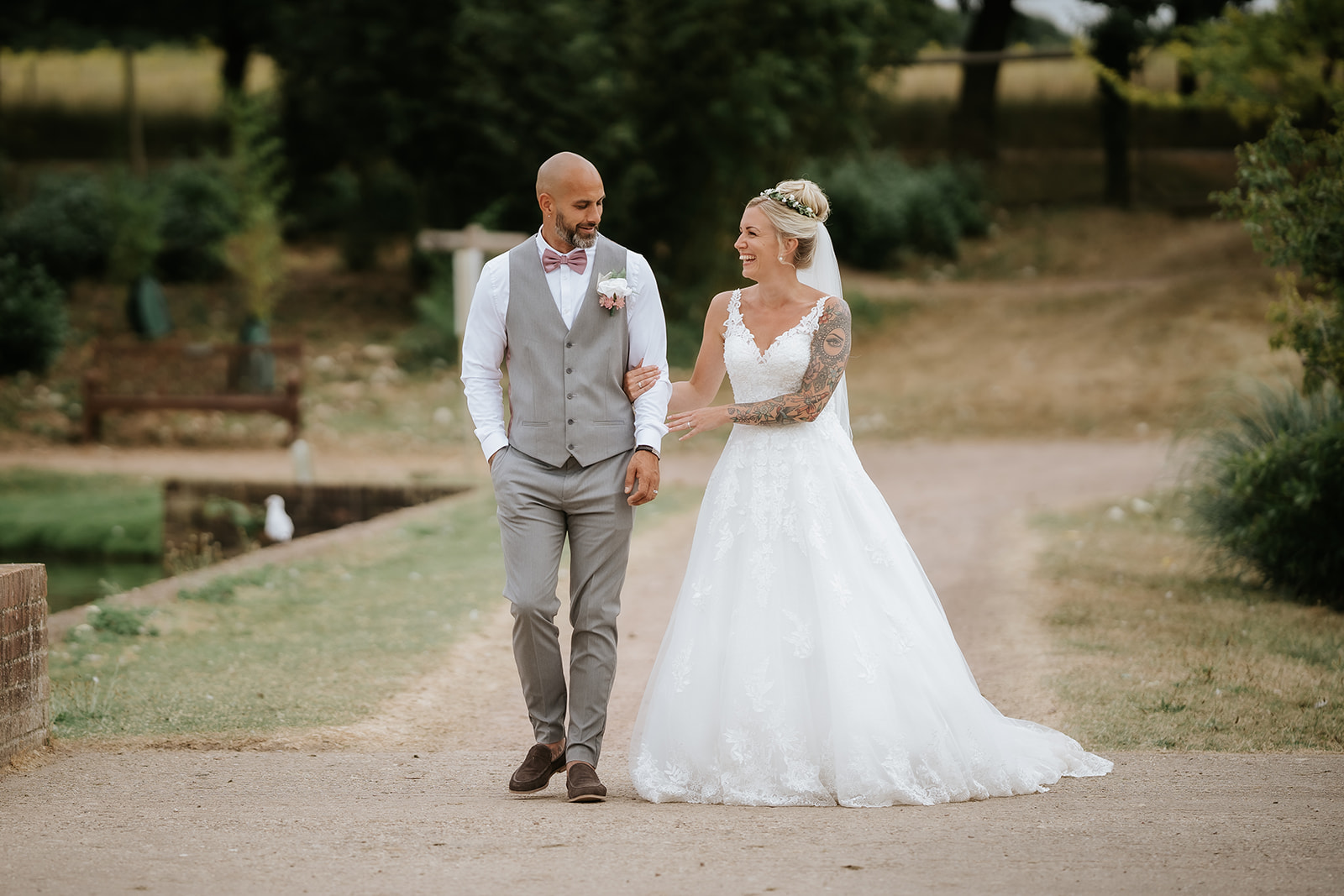 Bride and groom walking together laughing naturally in the countryside at Marks Hall Estate wedding near Colchester — candid documentary photography by Lily & White