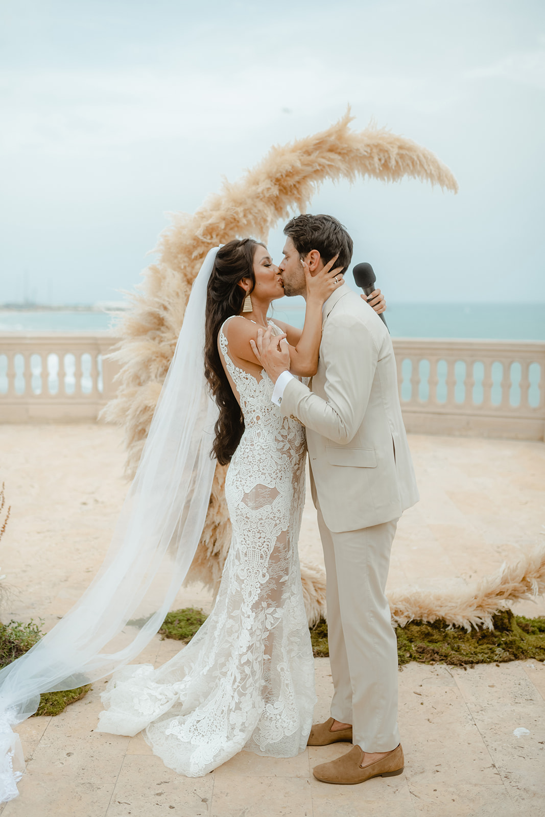Bride and groom under a floral arch by the sea at Xalet del Nin, Sitges
